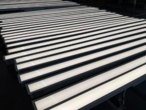 Fileiras de luminárias lineares de LED iluminadas em uma superfície de trabalho de produção.