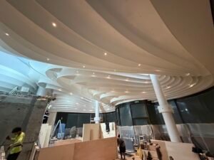 Intérieur d'un centre commercial en construction, avec un plafond à haut plafond, des formes blanches incurvées et des points lumineux intégrés.