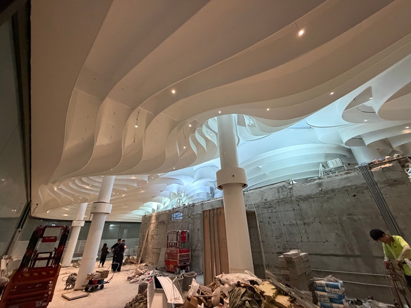 Intérieur d'un centre commercial en construction, avec un plafond à haut plafond, des formes blanches sculptées et des points lumineux intégrés.