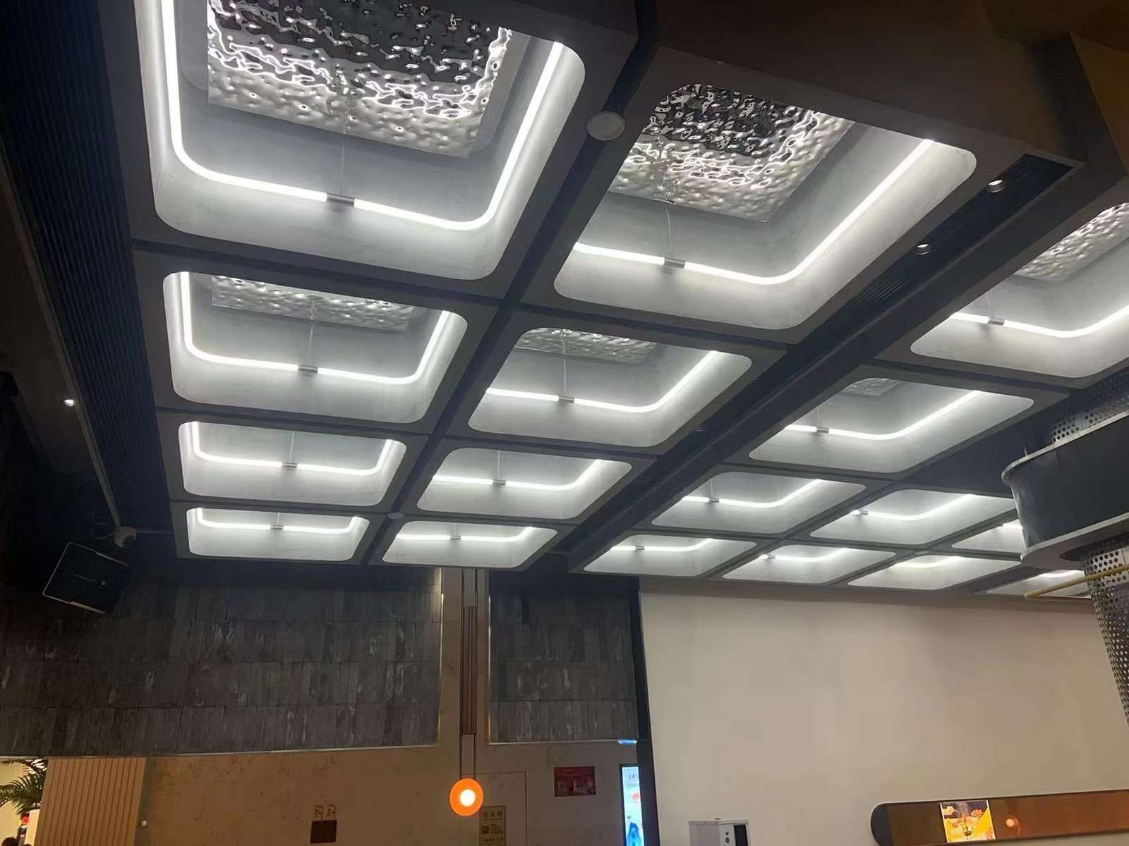 Gros plan sur des modules de tubes LED carrés à 360° répétés dans le même plafond commercial.